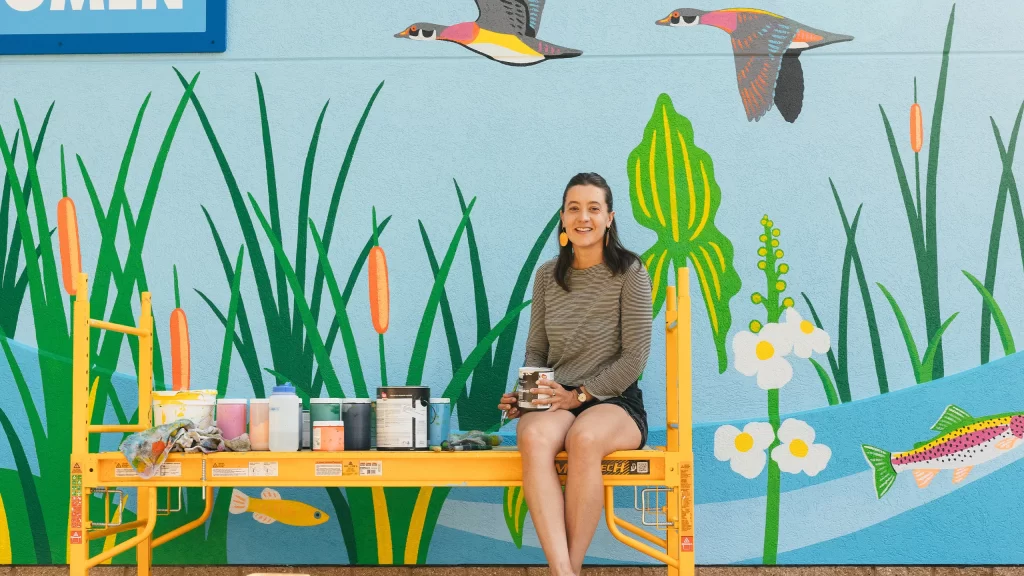 Artist Natalie Hinahara in front of the mural she painted at Bauman Community Pool in Middleton Wisconsin